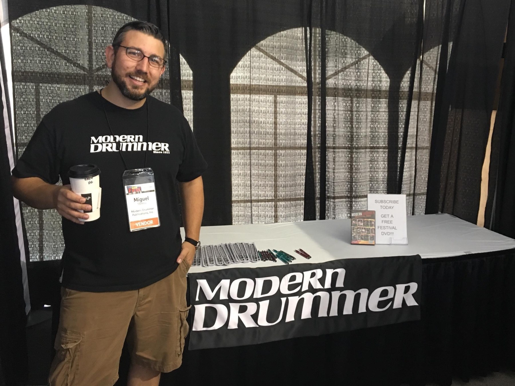 Miguel at a Modern Drummer booth, wearing a Modern Drummer shirt.